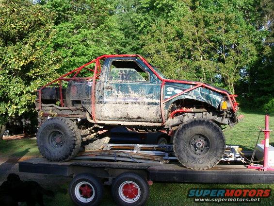 Mud-covered off-road truck with red roll cage on trailer