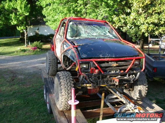 Modified off-road truck with red roll cage and cracked windshield on a trailer