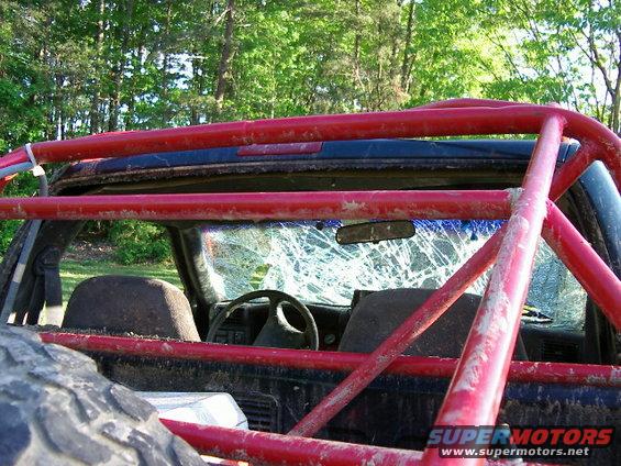 Interior view of a modified off-road vehicle with a red roll cage and a cracked windshield. Spare tire visible