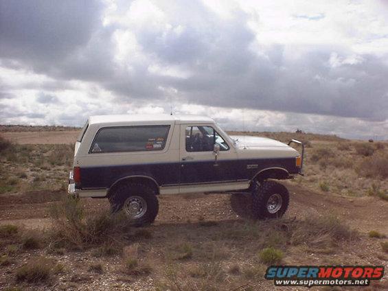 Two-tone white and dark blue Ford Bronco with lifted suspension and off-road tires on a dirt path