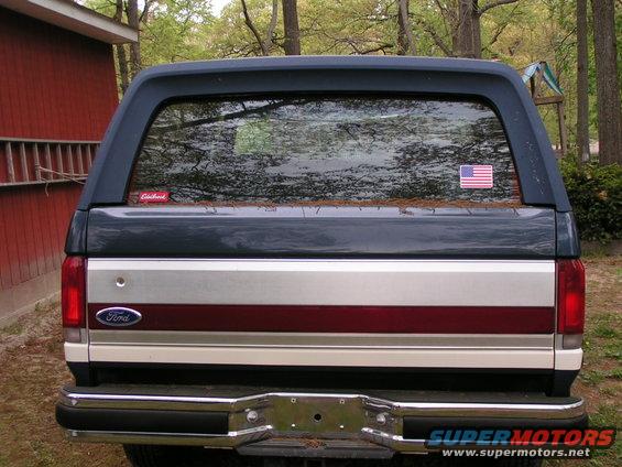 1987 Ford Bronco rear view, dark blue and silver body with red stripe, chrome bumper