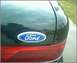 1992 Ford Crown Victoria - Close-up of a Ford emblem on the rear of a dark-colored vehicle.