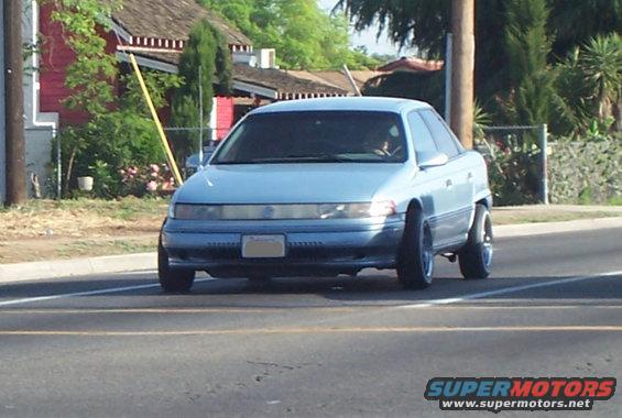 Light blue sedan, possibly a 1995 Mercury Sable, driving on a road