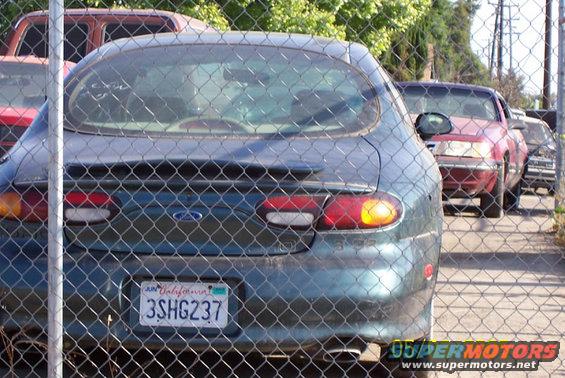 Rear of a teal Ford Taurus with a California license plate 3SHG237. Red car behind it