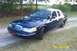 1998 Ford Crown Victoria - A dark blue sedan is parked on a dirt road with grass and trees surrounding it. The date 04/29/2005 is visible in the lower right corner.