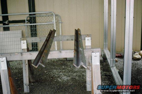 Metal beams on wooden supports, with a gate and construction framing in background