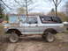 1979 Ford Bronco - This lifted Ford Bronco has a rusty hood and is parked on a dirt lot with a house in the background.