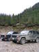 2000 Jeep Cherokee - Two SUVs are parked on a rocky surface with a dense forest and misty mountains behind them.