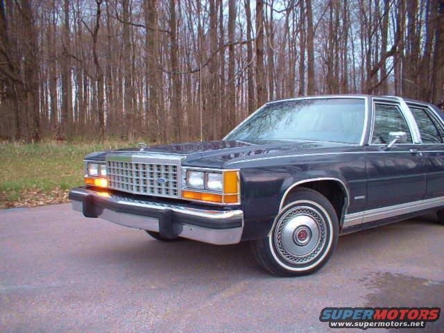 Dark blue sedan with chrome grille and bumper, parked on asphalt near trees