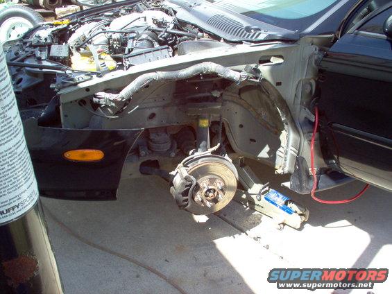 Car's front fender and engine compartment are open, showing disassembled parts and the engine