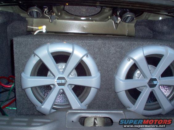 Two silver subwoofers in a car trunk with wiring
