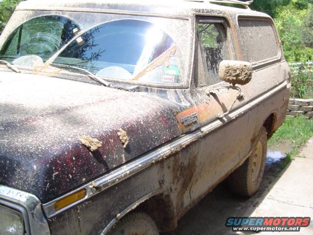 Mud-covered 1978 Ford Bronco, side view, showing dirt on hood, windshield, and side mirror