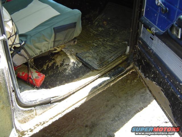 muddy floor mats and seats inside a vehicle, with a red fire extinguisher on the floor