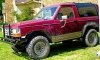 Maroon Ford Bronco II with aftermarket bumper and off-road tires parked on grass