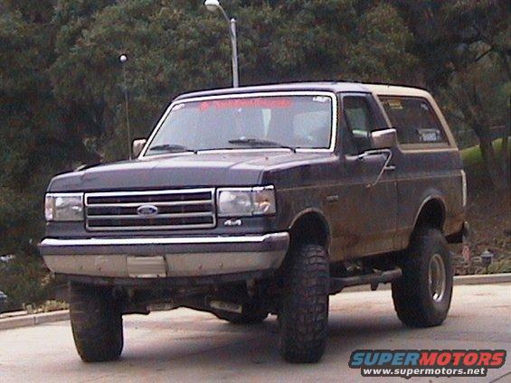 Dark blue Ford Bronco with a tan top, lifted suspension, and off-road tires, seen from a low front angle