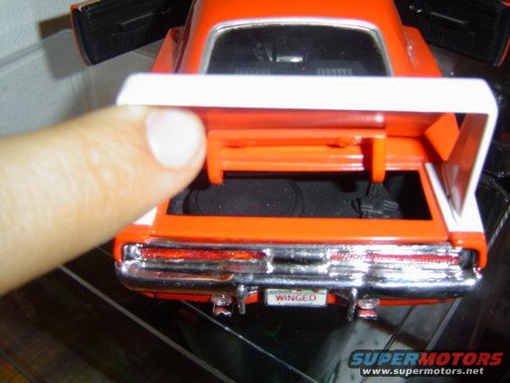Orange toy car trunk with white spoiler and 'WINGED' license plate. Finger is visible