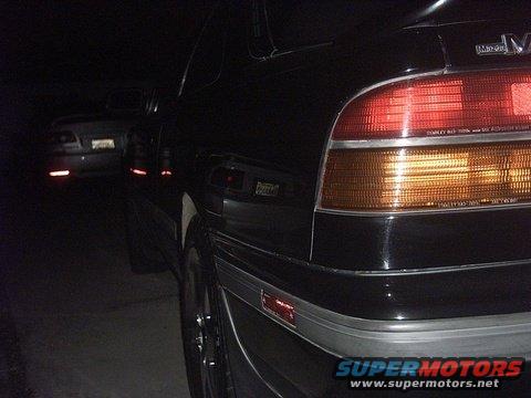 Black 1989 Mazda MX-6 GT 4WS rear quarter panel and taillight, with another car visible in the background