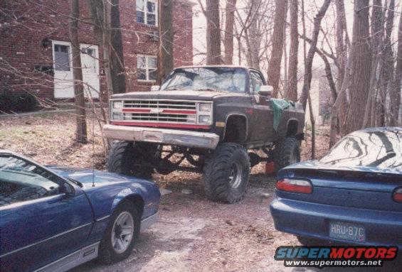 Lifted dark brown pickup truck with red grille trim, large tires, parked outdoors