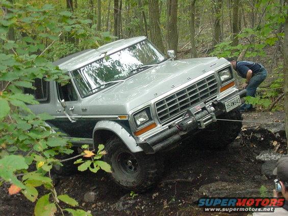 Silver 1978 Ford Bronco navigating a wooded trail with a person adjusting a winch cable