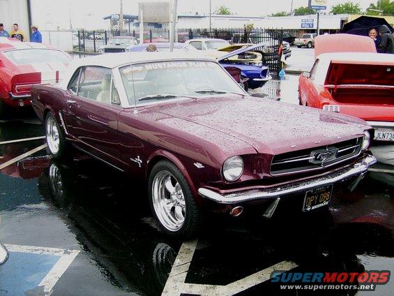 Maroon 1965 Ford Mustang convertible with a white top parked in the rain