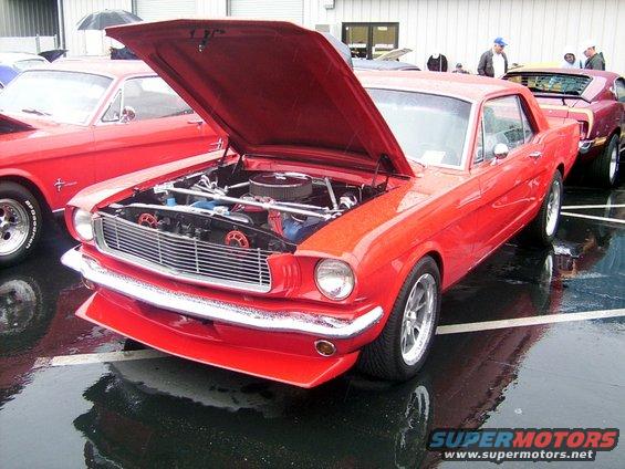 Red 1965 Ford Mustang coupe, hood open, parked on wet asphalt