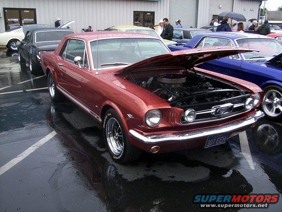 Red 1965 Ford Mustang coupe with hood open, parked next to other cars