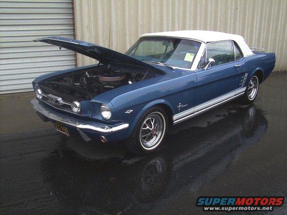 Blue 1965 Mustang convertible with white top, hood open, parked on wet pavement
