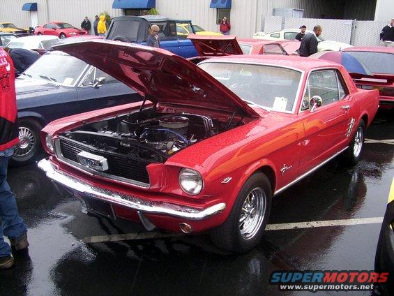 Red classic coupe with hood open, parked next to a dark blue car. Other vehicles and people visible in background