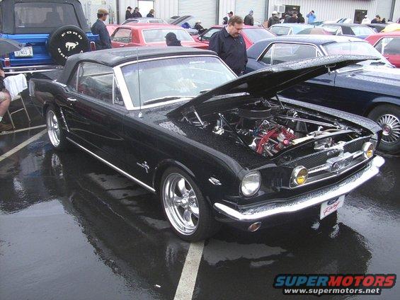 Black 1965 Mustang convertible with hood open, parked outside on a wet day. Other cars visible