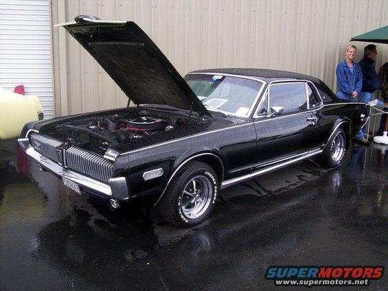 Black 1969 Mercury Cougar XR7 coupe with hood open, showing engine. Chrome grille, side trim, and wheels are visible