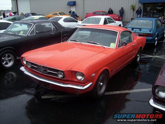 Red 1965 Ford Mustang coupe parked in lot with other cars