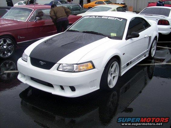 White Saleen Mustang with black hood and side graphics, parked on wet pavement