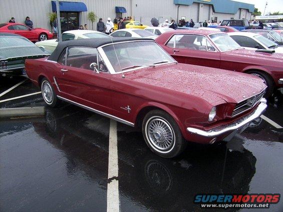 Red 1965 Mustang convertible parked on wet asphalt, other cars nearby