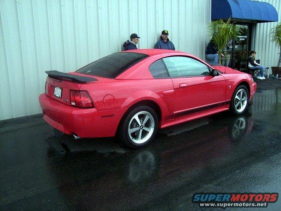 Red 2002 Ford Mustang coupe parked on wet asphalt, viewed from the rear three-quarter angle