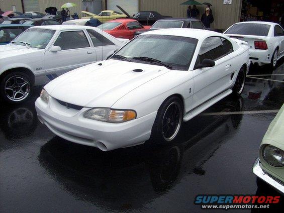 White Ford Mustang SN95 generation parked on wet asphalt, other cars visible