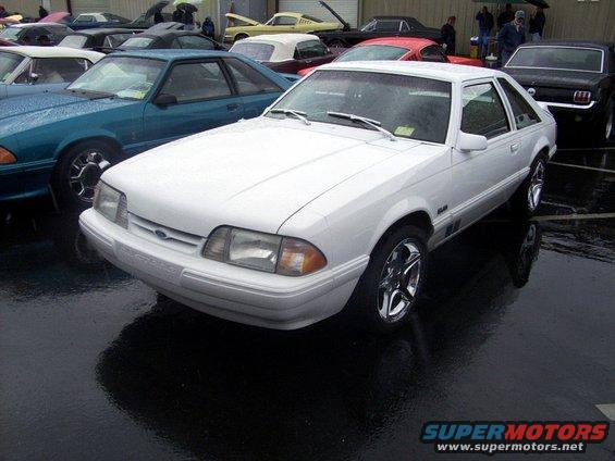 White Ford Mustang hatchback parked on wet asphalt, other cars around