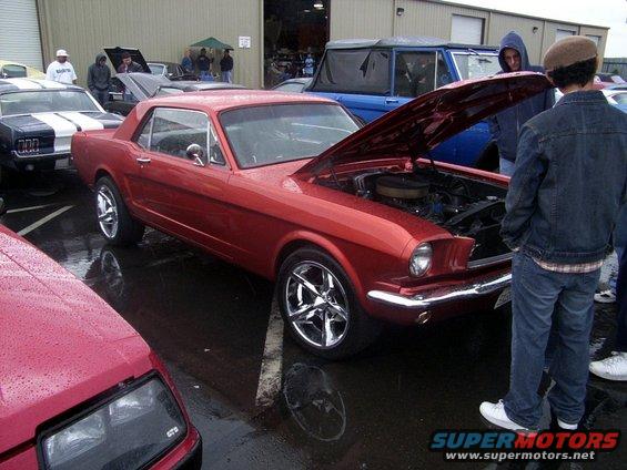 Red 1965 Ford Mustang coupe with hood open, showing engine