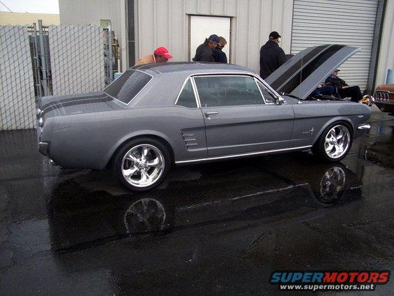 Gray 1965 Ford Mustang coupe with black racing stripes on hood and trunk, chrome wheels, hood open
