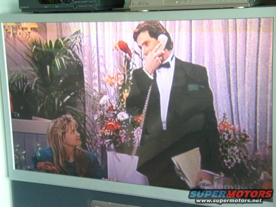 Television screen displaying a scene with a man in a tuxedo on the phone and a young woman looking on