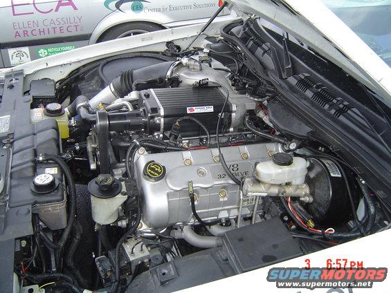 Engine bay with V8 32 valve engine and a black supercharger. Text on a nearby vehicle reads 'ELLEN CASSILY ARCHITECT'