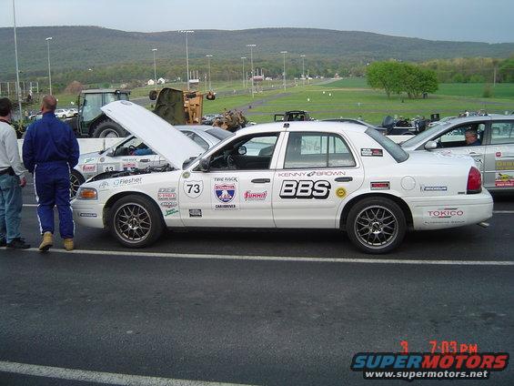 1999 Ford Crown Victoria race car with BBS decals and number 73, hood open. Another car visible behind it