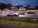 1999 Ford Crown Victoria - A white 1999 Ford Crown Victoria, adorned with racing decals, competes on a track at dusk alongside another vehicle.