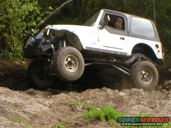 White Jeep Wrangler with a black top navigating rocky terrain, front left wheel lifted