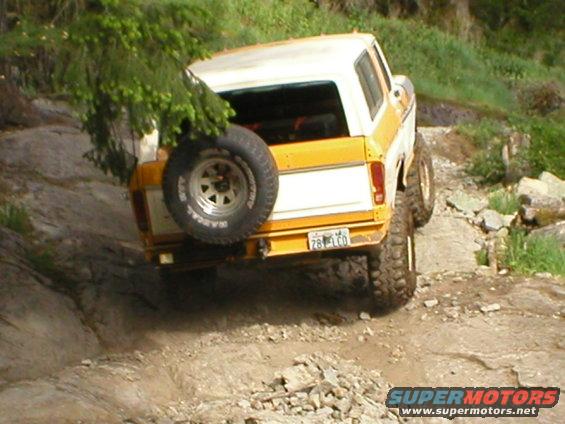 Rear view of a yellow and white 1978 Ford Bronco off-roading on a rocky trail