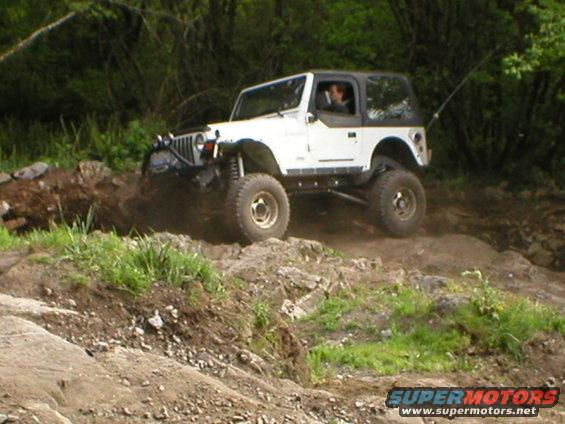 White Jeep Wrangler with a black top driving off-road over rocks and dirt