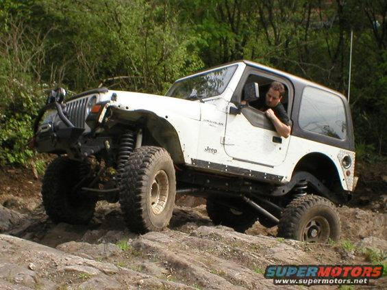 White Jeep Wrangler climbing rocks, driver visible
