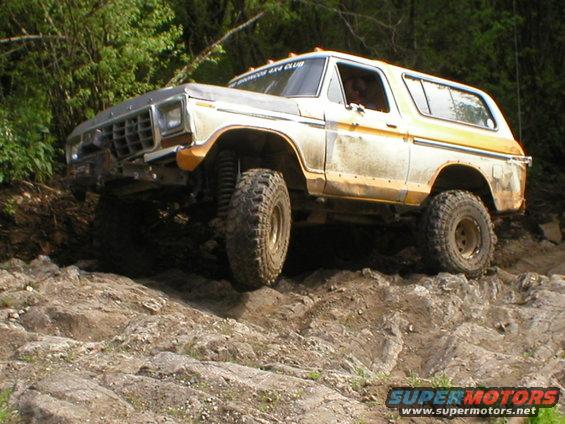 Yellow and white 1978 Ford Bronco off-roading on rocks, front left tire elevated