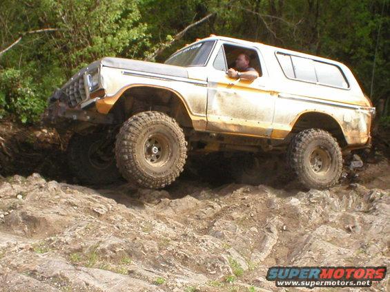 Yellow and white 1978 Ford Bronco off-roading on a rocky incline, front right wheel elevated