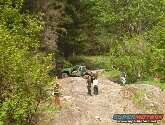 Off-road vehicles navigating a rocky trail with people watching