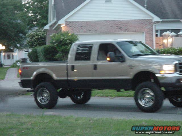 Pickup truck driving on a road, side view. It has large tires and a two-tone paint job